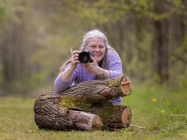 yvonne van leeuwen achter een houtblok in het bos met fototoestel in haar handen
